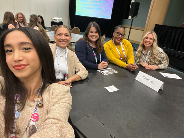Group of Hygiene Students in business attire sitting at a table in a conference room taking a selfie